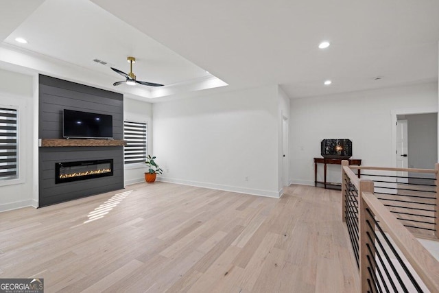 living room with ceiling fan, light wood-style flooring, recessed lighting, a large fireplace, and a tray ceiling