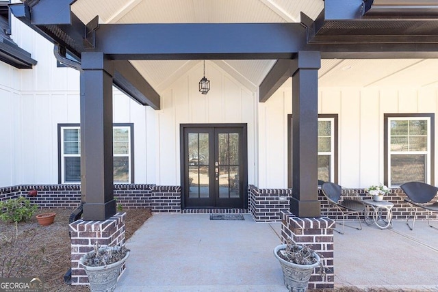 view of exterior entry with board and batten siding, french doors, and brick siding