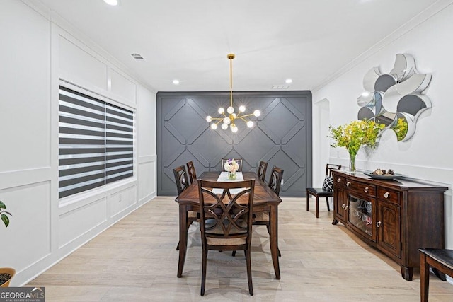 dining area featuring crown molding, light wood finished floors, a decorative wall, an inviting chandelier, and an accent wall