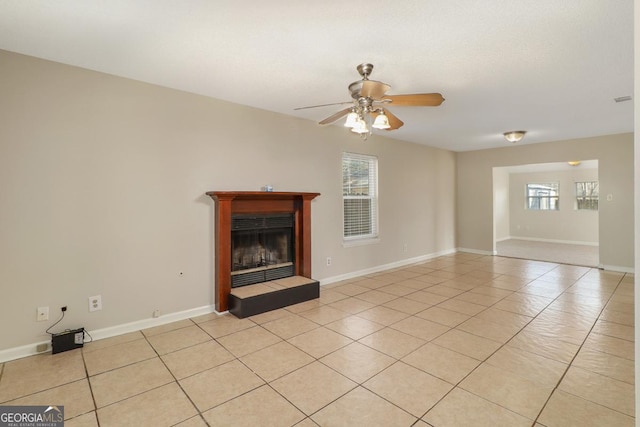 unfurnished living room with a ceiling fan, a healthy amount of sunlight, a fireplace with raised hearth, and light tile patterned flooring