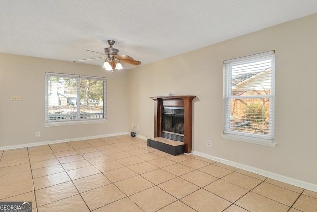 unfurnished living room with light tile patterned floors, ceiling fan, a fireplace, and baseboards