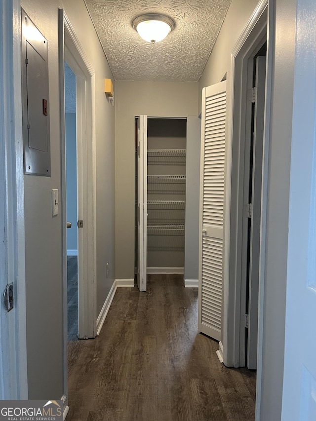 corridor with a textured ceiling, wood finished floors, electric panel, and baseboards