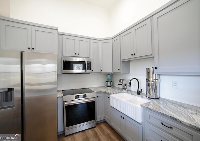 kitchen featuring dark wood finished floors, stainless steel appliances, gray cabinets, a sink, and light stone countertops