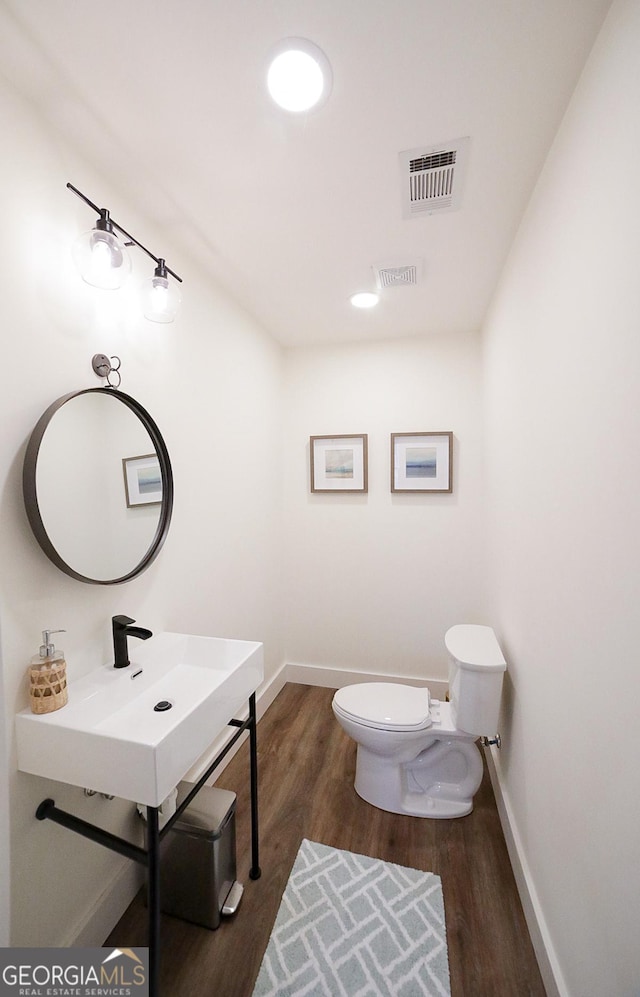 half bathroom with toilet, baseboards, visible vents, and wood finished floors