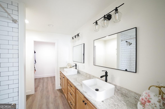 full bathroom featuring double vanity, a tile shower, a sink, and wood finished floors