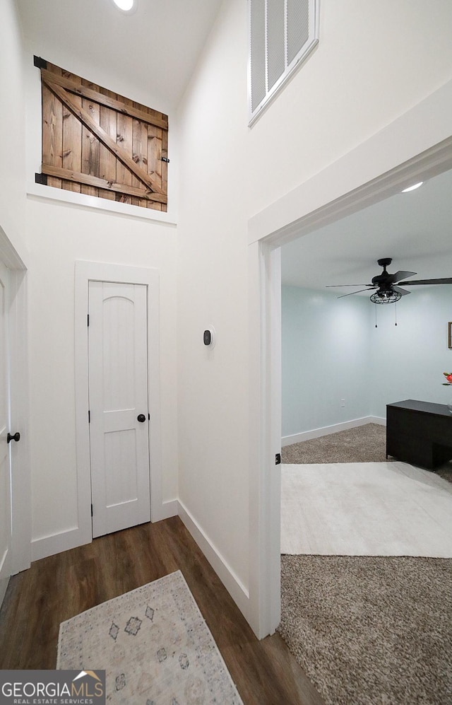 entryway featuring baseboards, visible vents, ceiling fan, wood finished floors, and a high ceiling