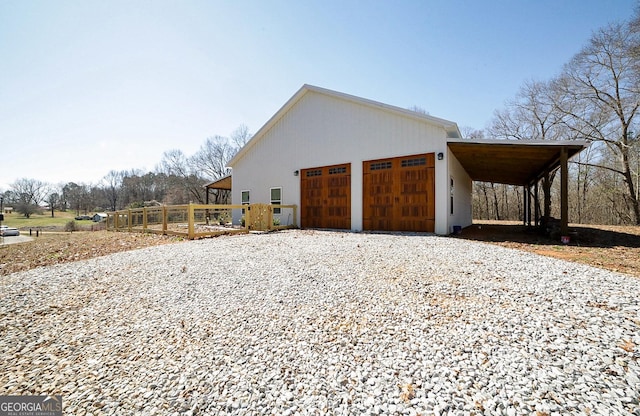 garage with driveway, fence, and a carport