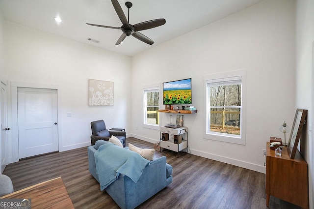 living area featuring visible vents, a towering ceiling, ceiling fan, wood finished floors, and baseboards