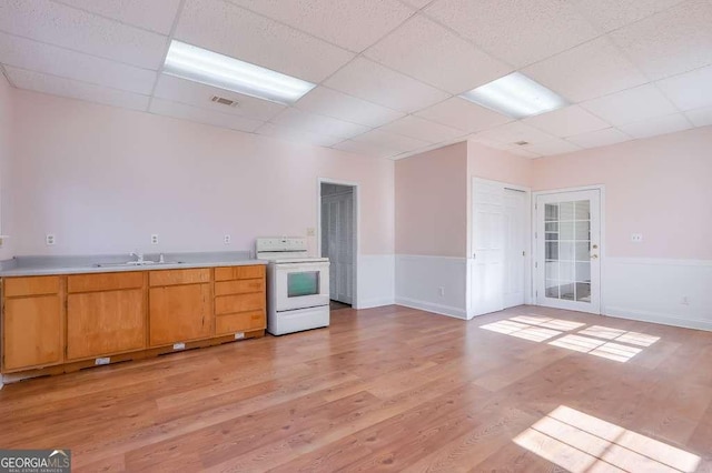 kitchen featuring light wood finished floors, electric range, a drop ceiling, light countertops, and a sink