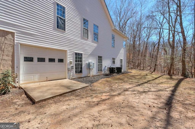 view of side of property featuring driveway, central AC unit, and an attached garage