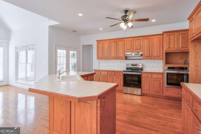 kitchen featuring stainless steel appliances, a sink, tile counters, and under cabinet range hood