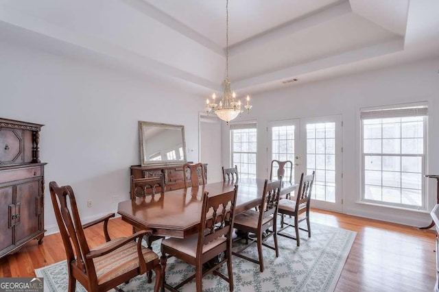 dining room featuring french doors, a notable chandelier, a raised ceiling, light wood-style floors, and baseboards