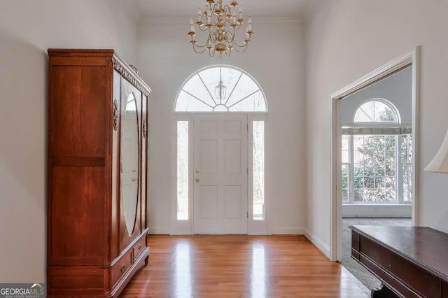 foyer with ornamental molding, light wood finished floors, and a notable chandelier