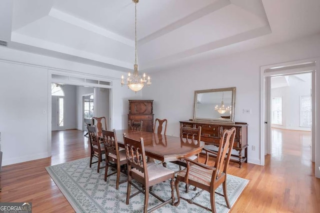 dining room featuring light wood finished floors, baseboards, visible vents, a raised ceiling, and a notable chandelier