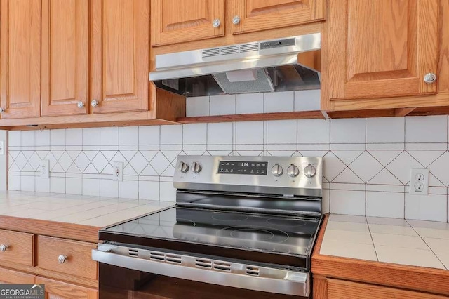 kitchen featuring under cabinet range hood, tasteful backsplash, tile counters, and electric stove