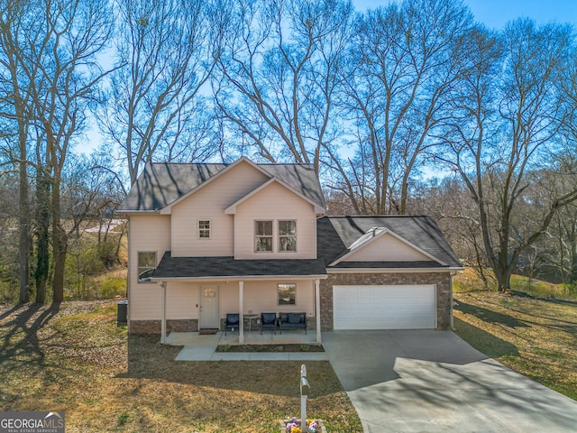 traditional-style house featuring a porch, a garage, driveway, stone siding, and a front yard