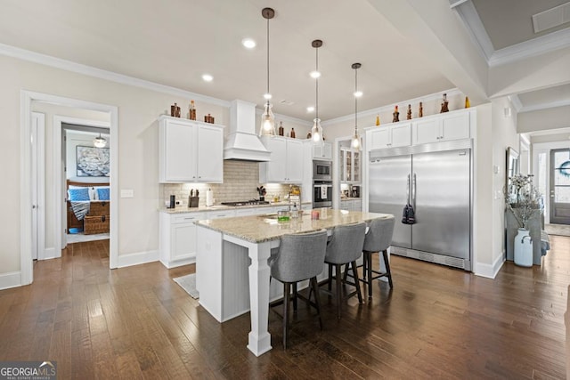 4590 Gablestone Xing, Hoschton, GA 30548 - kitchen with built in appliances, custom range hood, ornamental molding, decorative backsplash, and a center island with sink