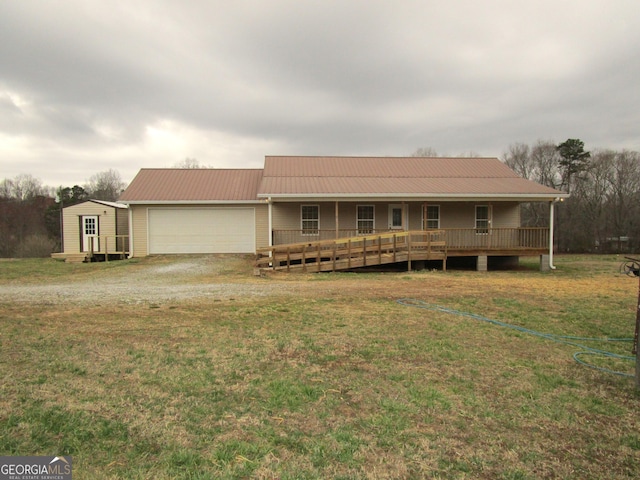 view of front facade featuring dirt driveway, metal roof, an attached garage, covered porch, and a front yard