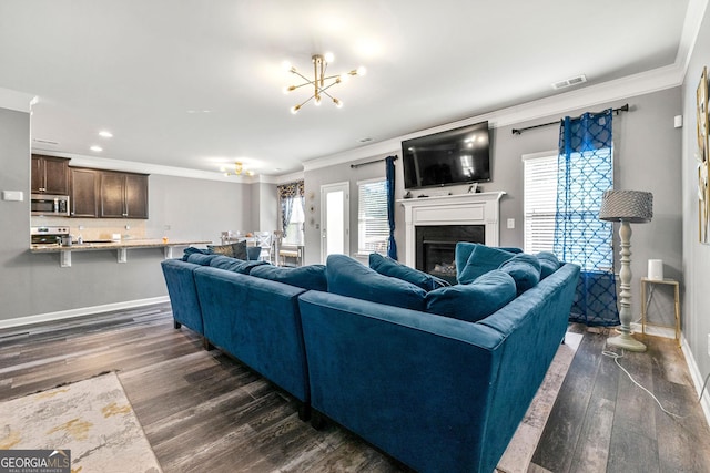 living room featuring a notable chandelier, dark wood-type flooring, visible vents, a glass covered fireplace, and crown molding