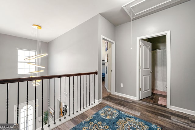 hallway with an inviting chandelier, attic access, baseboards, and wood finished floors