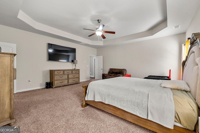 bedroom with a tray ceiling, carpet, visible vents, a ceiling fan, and baseboards