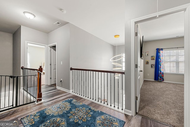 corridor featuring visible vents, baseboards, wood finished floors, and an upstairs landing