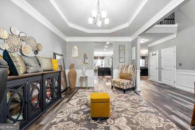 living area with wood finished floors, wainscoting, an inviting chandelier, a raised ceiling, and crown molding