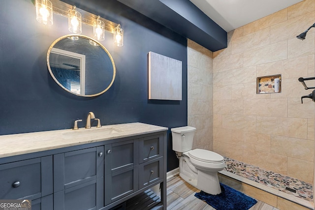 bathroom with baseboards, a tile shower, vanity, and toilet