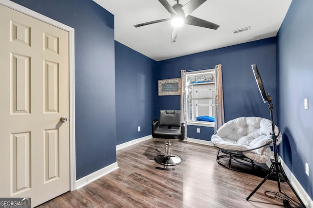 living area featuring a ceiling fan, visible vents, baseboards, and wood finished floors