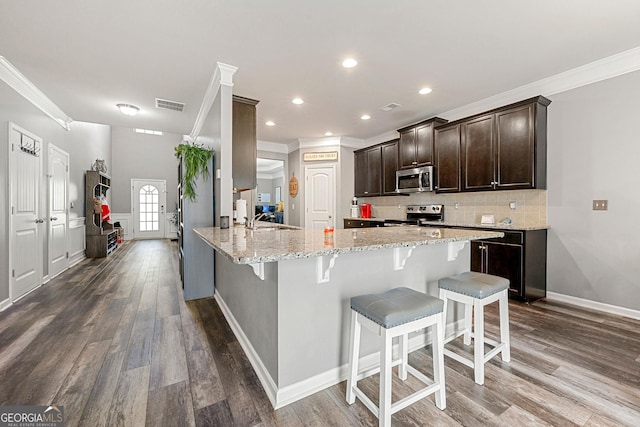 kitchen featuring a breakfast bar, visible vents, backsplash, appliances with stainless steel finishes, and dark brown cabinets