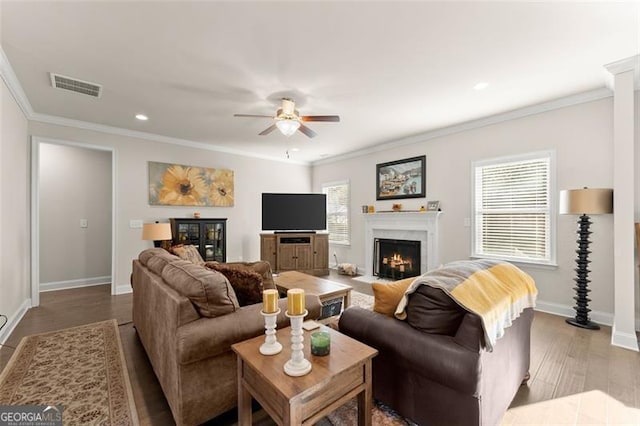 living area featuring wood finished floors, a fireplace with flush hearth, baseboards, visible vents, and crown molding