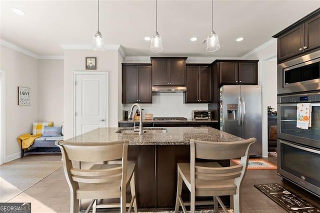 kitchen with light stone countertops, stainless steel appliances, dark brown cabinets, under cabinet range hood, and a sink