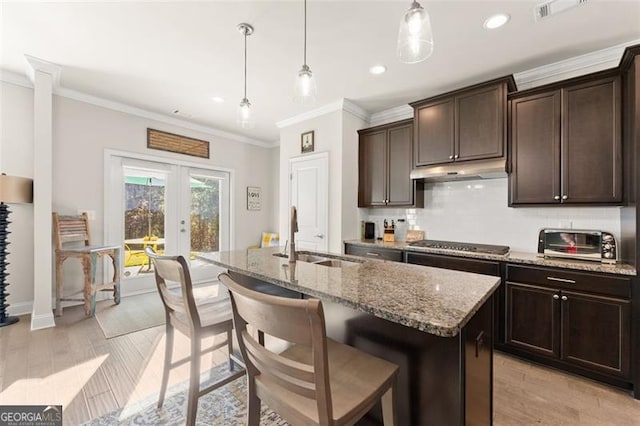 kitchen featuring light stone counters, french doors, stainless steel gas stovetop, a sink, and under cabinet range hood