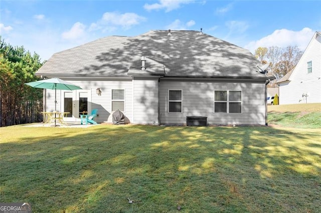 rear view of house featuring a patio, a shingled roof, and a lawn