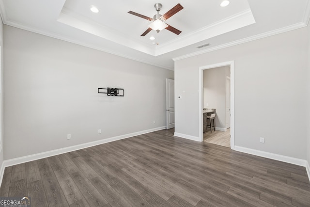 unfurnished bedroom featuring dark wood-type flooring, visible vents, baseboards, a tray ceiling, and crown molding