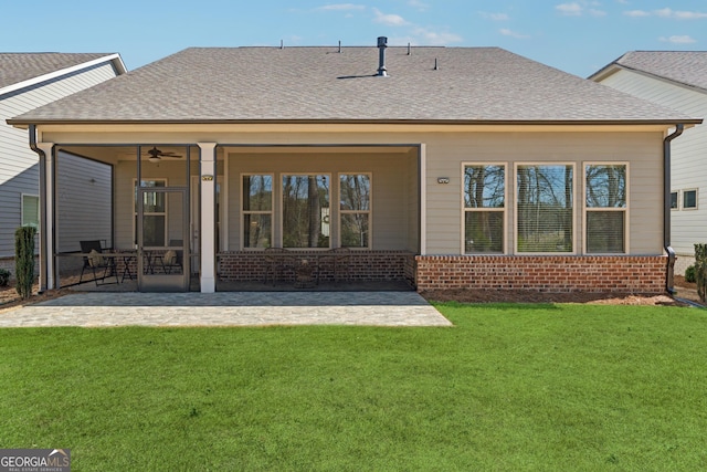 rear view of property featuring a patio, brick siding, a sunroom, roof with shingles, and a lawn