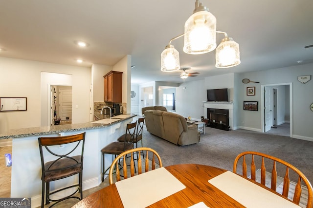 carpeted dining room featuring a fireplace, a sink, visible vents, a ceiling fan, and baseboards