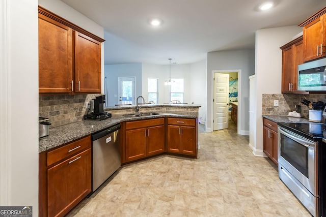 kitchen featuring backsplash, appliances with stainless steel finishes, a sink, dark stone countertops, and a peninsula