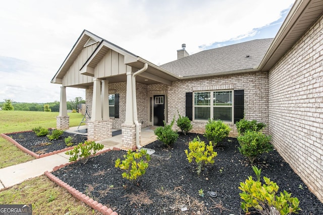 property entrance with brick siding, a shingled roof, a lawn, board and batten siding, and a patio area