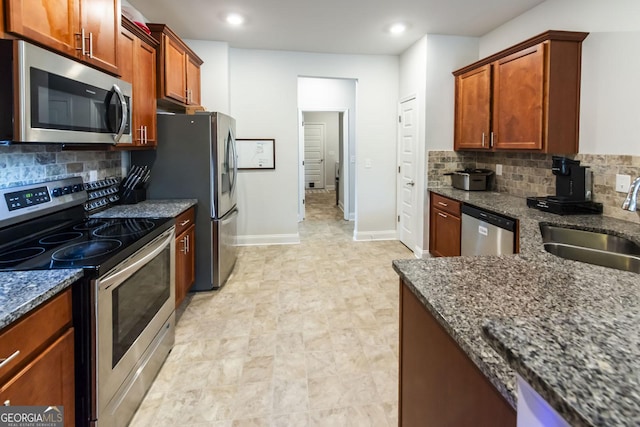 kitchen featuring appliances with stainless steel finishes, dark stone counters, a sink, and baseboards