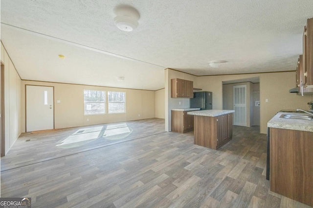 kitchen with open floor plan, brown cabinets, a center island, freestanding refrigerator, and a sink