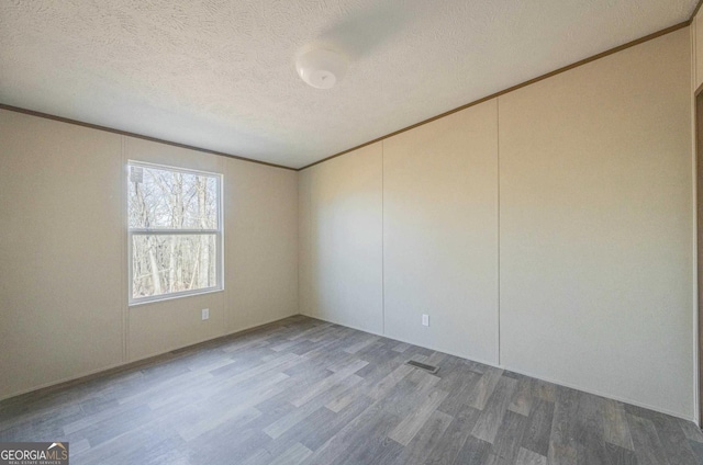 empty room featuring visible vents, crown molding, a textured ceiling, and wood finished floors