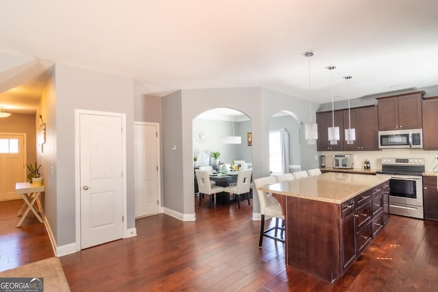 kitchen featuring stainless steel appliances, a breakfast bar, dark wood-style flooring, and light stone counters