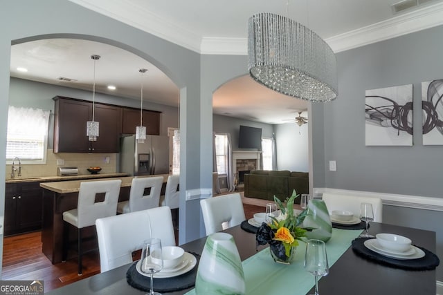 dining room with a stone fireplace, visible vents, dark wood-type flooring, and ornamental molding