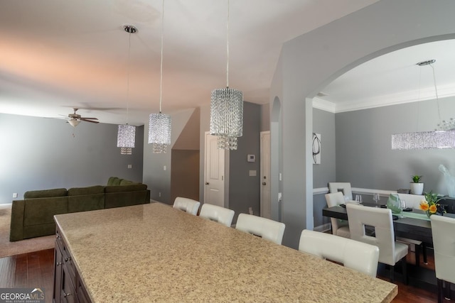 kitchen with arched walkways, a breakfast bar, open floor plan, dark wood-type flooring, and ceiling fan with notable chandelier