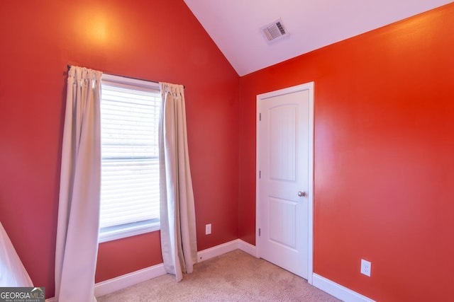 empty room with light carpet, vaulted ceiling, visible vents, and baseboards