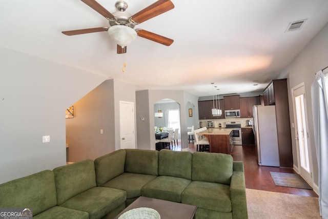 living room featuring a ceiling fan, arched walkways, dark wood-style flooring, and visible vents