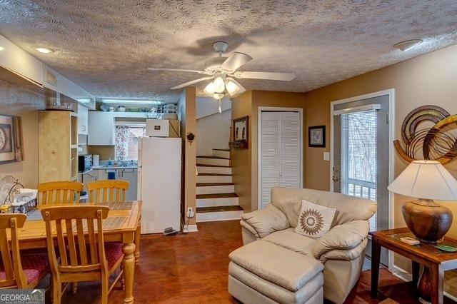 sitting room with ceiling fan, stairway, and a textured ceiling