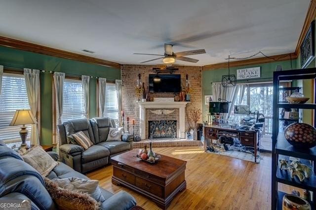 living room with ceiling fan, a brick fireplace, wood finished floors, and visible vents