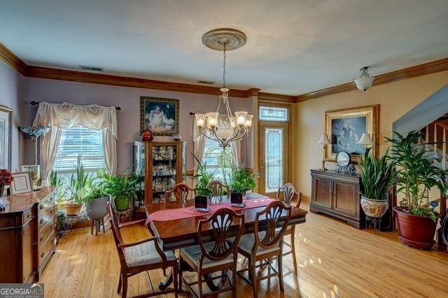 dining space featuring light wood-type flooring, visible vents, ornamental molding, and a chandelier